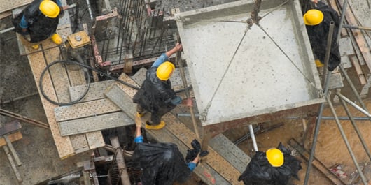 4 ouvriers avec des casques de chantier, coulant du ciment sous la pluie_600x300_blog